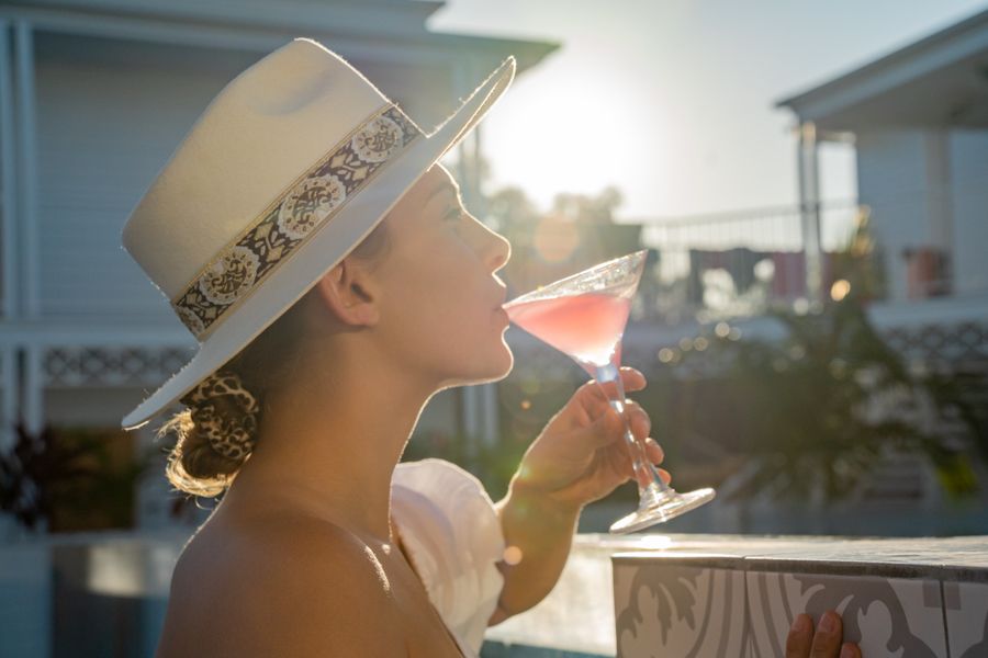 A girl wearing a white broad brimmed hat sipping a pink cocktail