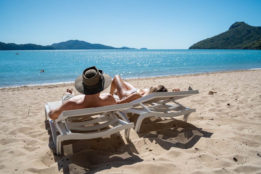 A man and a woman lying on lounge chairs on the beach