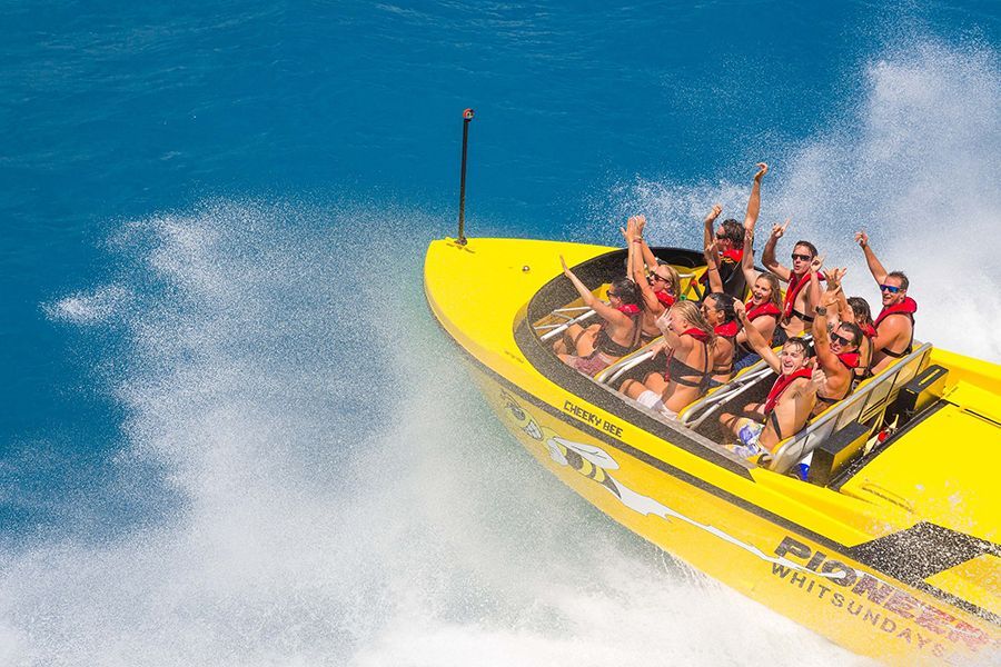 People in a jetboat with red life jackets on with hands in the air