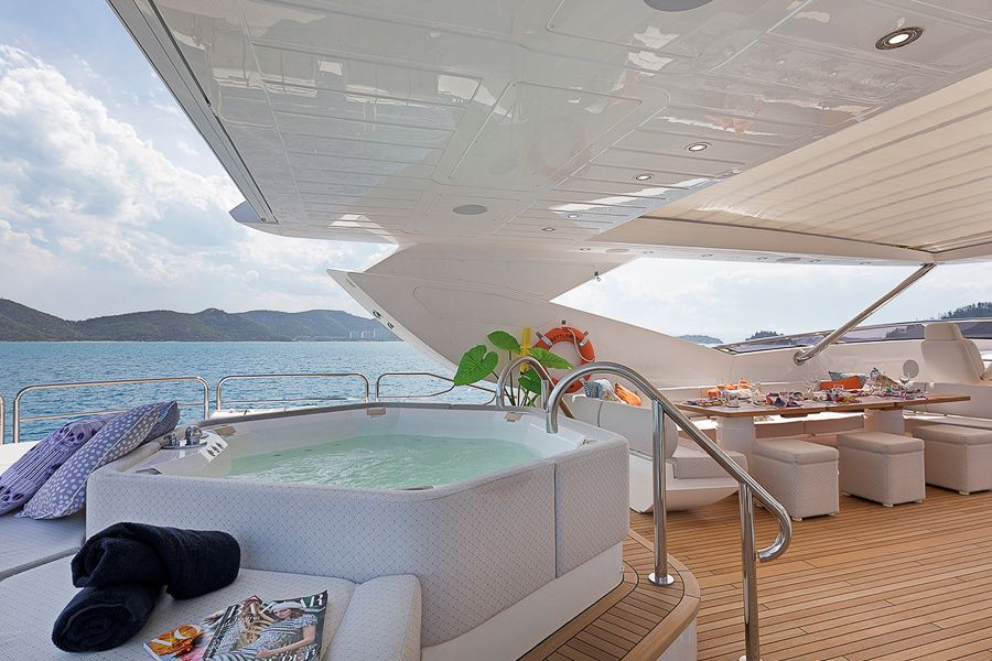 A jacuzzi on the back of a yacht surrounded by white furnishings and the ocean 