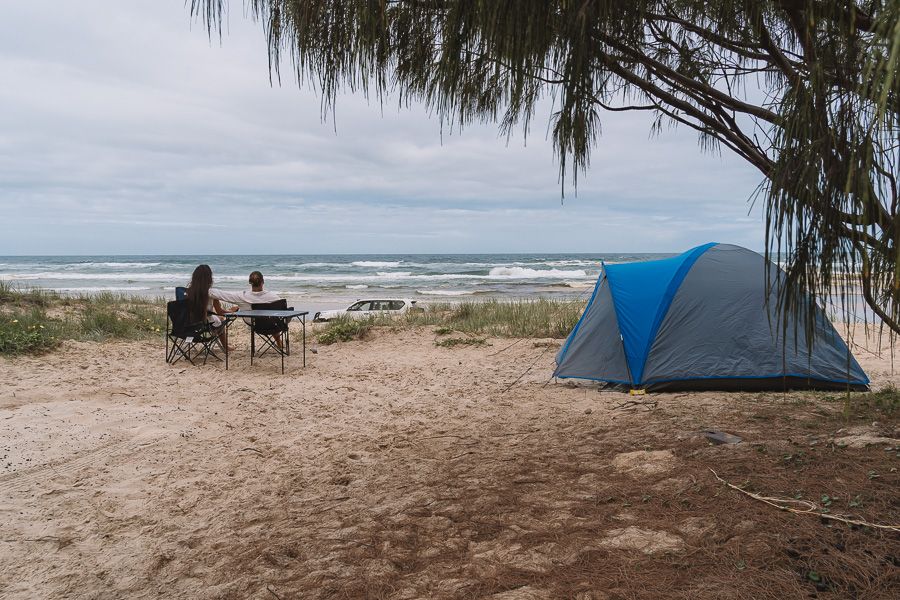 two travellers sitting in beach chairs at a beachfront K'gari campsite