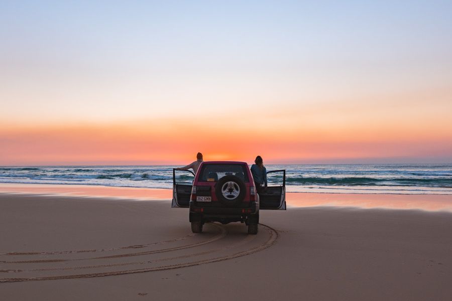 Travellers in a 4WD by the beach at sunrise on K'gari