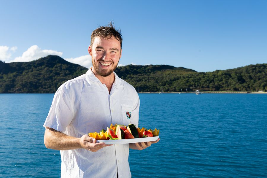 Working In The Whitsundays a man holding a platter of fruit on a boat in the whitsundays