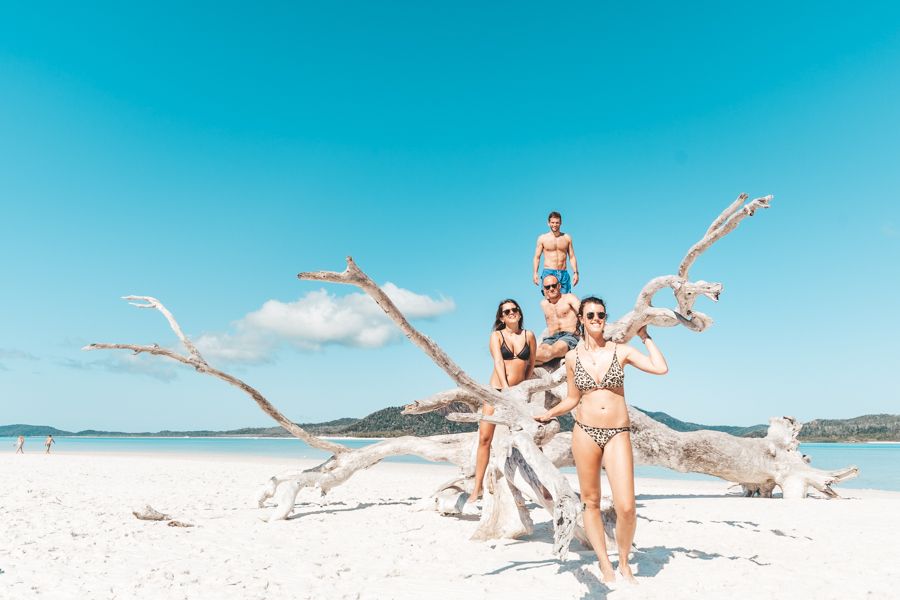 Travellers posing with driftwood on Whitehaven Beach Whitsunday island