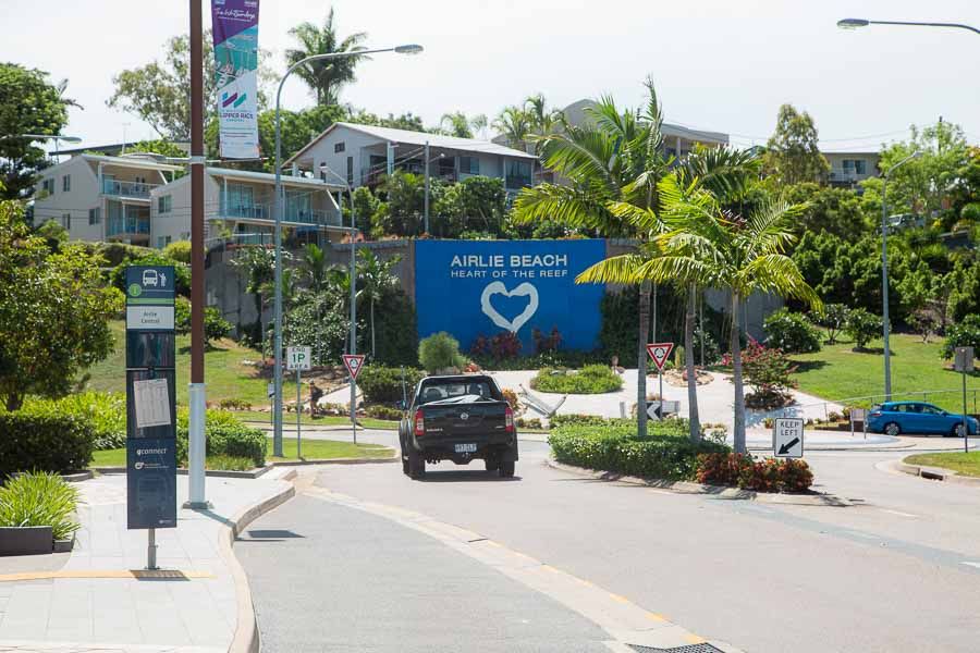 The main street of a Airlie Beach with a car, roundabout and a blue sign