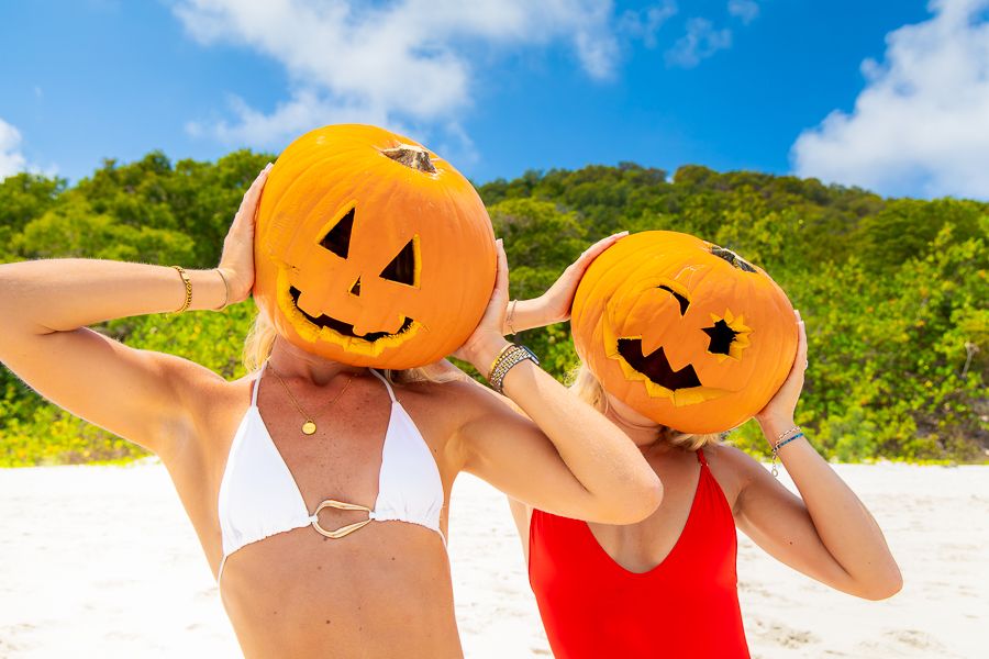 Halloween in Airlie Beach 2025 two women in bikinis on a beach with pumpkins on their heads