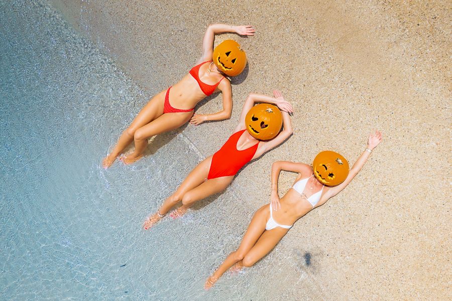 Airlie Beach, Queensland Three girls in bikinis laying on the sand with pumpkins on their heads