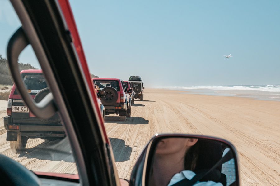 A convoy of 4WDs driving along the sand on K'gari