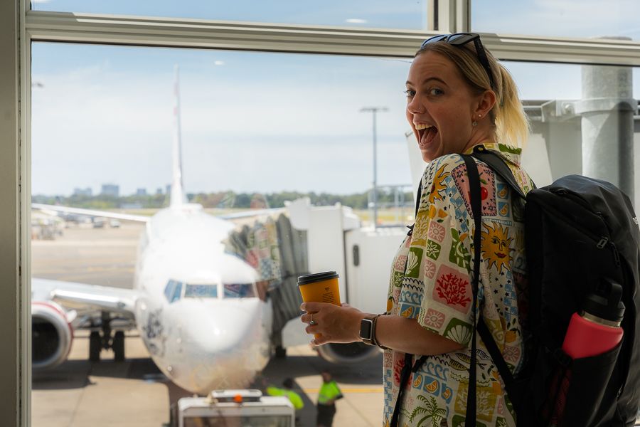 girl with a coffee and bag smiling at an airport
