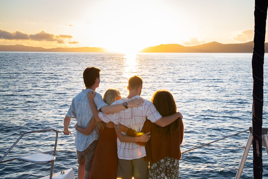 people posing in front of sunset on a sailing catamaran
