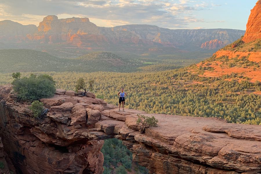 Woman standing on natural stone bridge overlooking desert valley