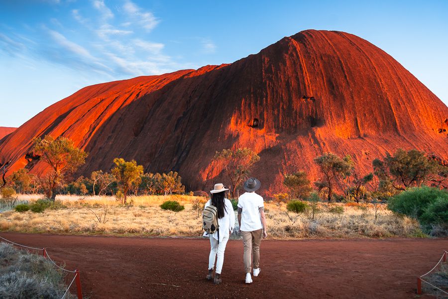 couple walking in front of uluru red rock face