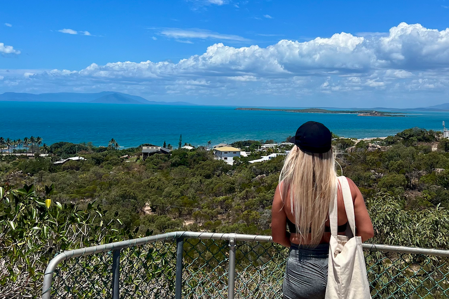 A woman with long blonde hair standing at a lookout over the ocean