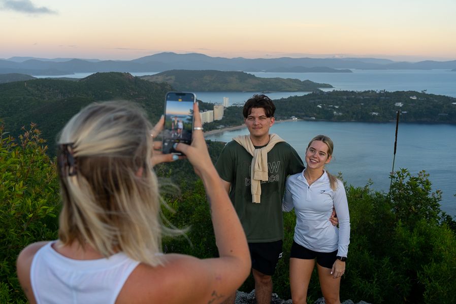 A woman taking a photo of a couple at a lookout