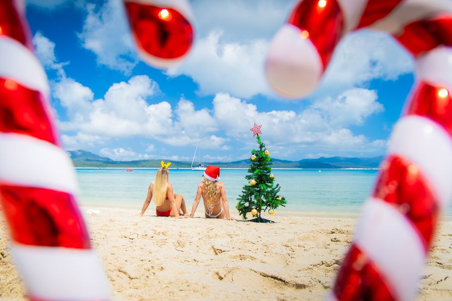 two women wearing santa hats sitting on the beach