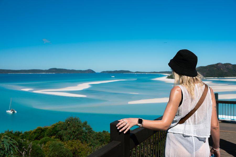 Where is the Whitsundays located? a woman standing at hill inlet lookout overlooking the ocean