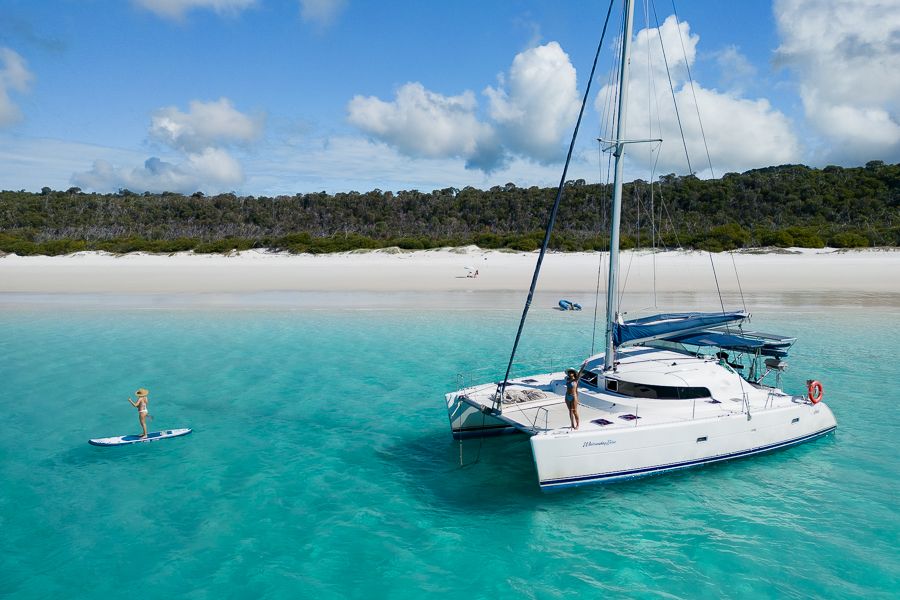 a drone shot of a catamaran in front of a beach