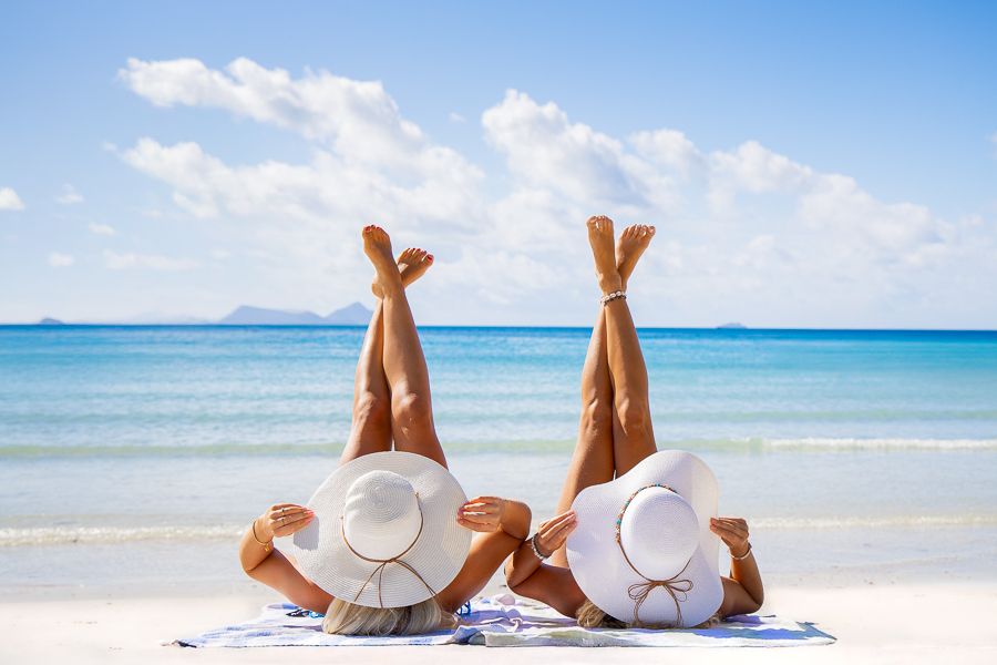 Two women lying on white sand with her legs in the air